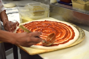 A chef spreading pizza sauce on pizza dough