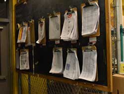 a wall with multiple clipboards full of papers hanging on it