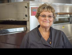 Photo of Ann standing in front of her ovens smiling